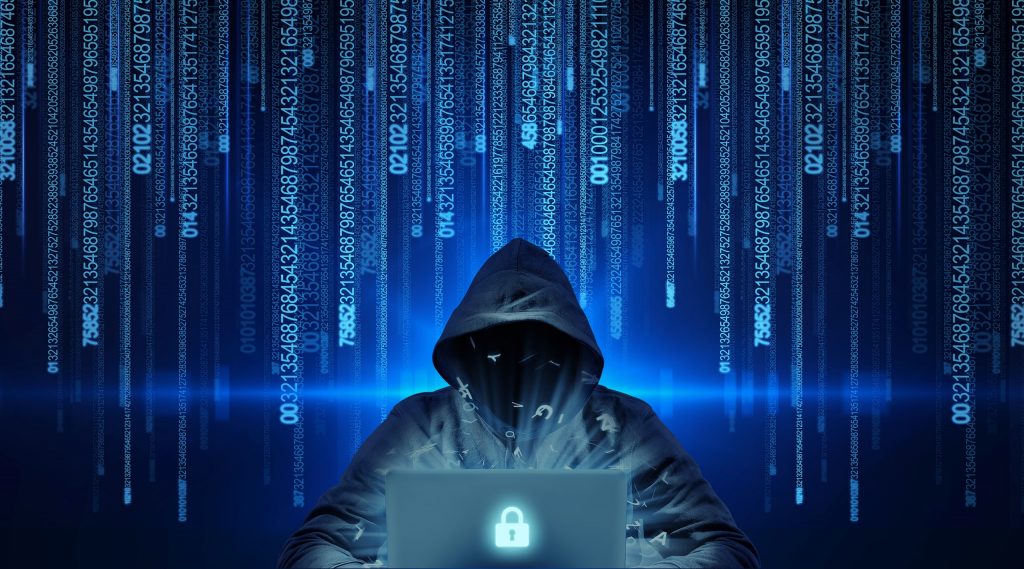 Pessoa com capuz atrás de um notebook