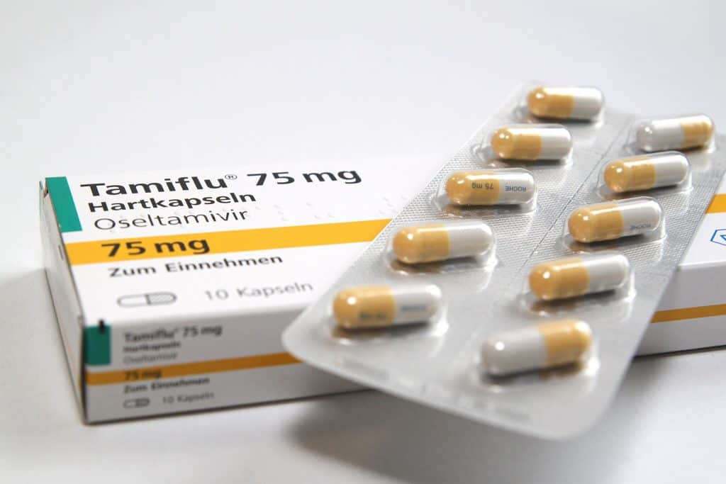 Embalagem do medicamento Tamiflu de 75 mg com cápsulas em um blister. A embalagem apresenta texto em alemão, destacando "Hartkapseln" e "Oseltamivir". Dez cápsulas amarelas e brancas estão visíveis fora da embalagem.