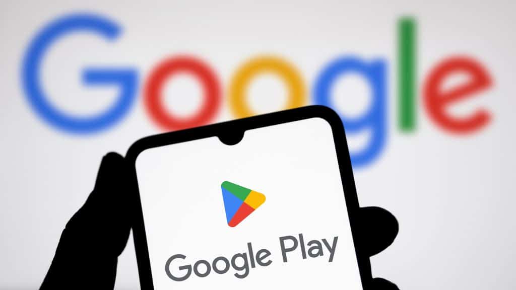 Pessoa segurando celular com imagem de logotipo da Google Play Store e, ao fundo, a logomarca do Google