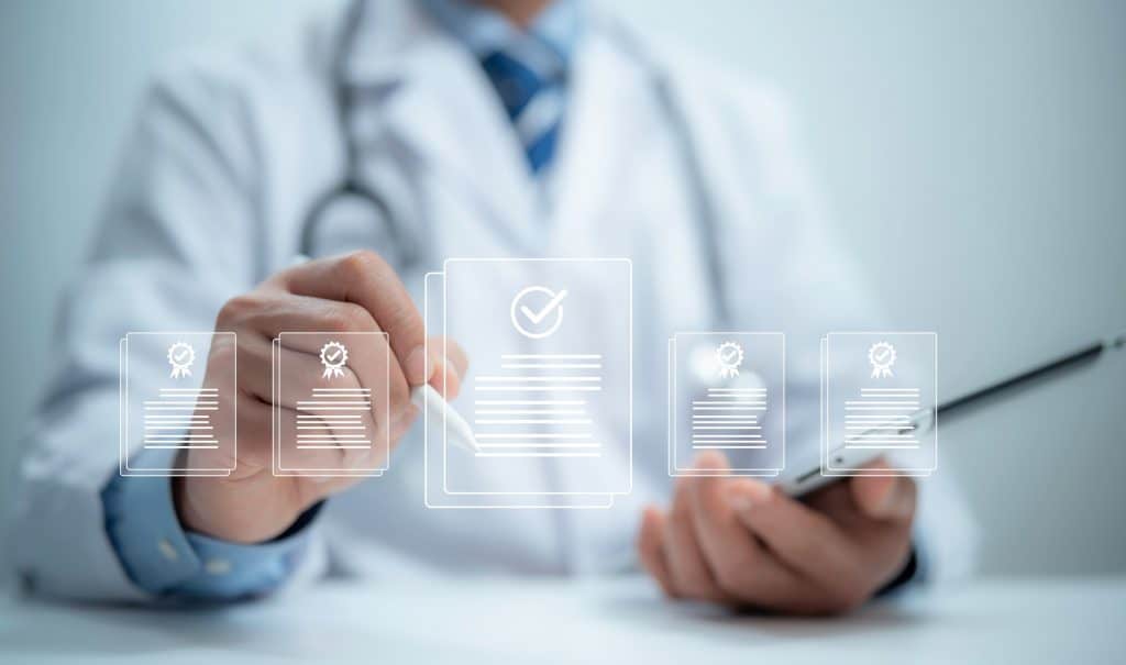 Médico com um tablet na mão e selecionando, no ar, um ícone de documento com uma caneta