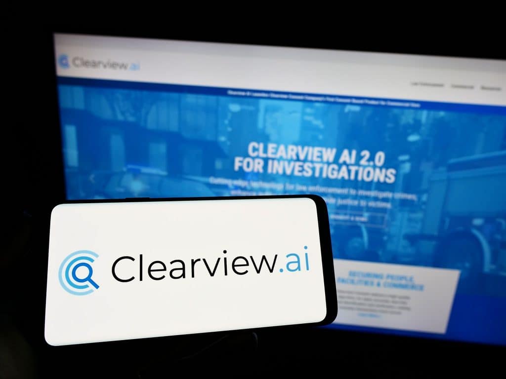 Logo da Clearview AI em um smartphone, com o site da empresa ao fundo em uma tela de computador