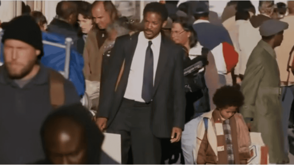 Homem alto negro de terno com criança no meio de multidão (cena do filme A procura da felicidade)