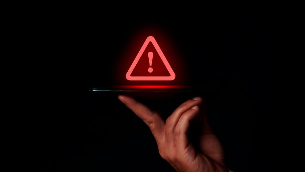 Pessoa segurando celular com ilustração de sinal de alerta vermelho em cima do aparelho