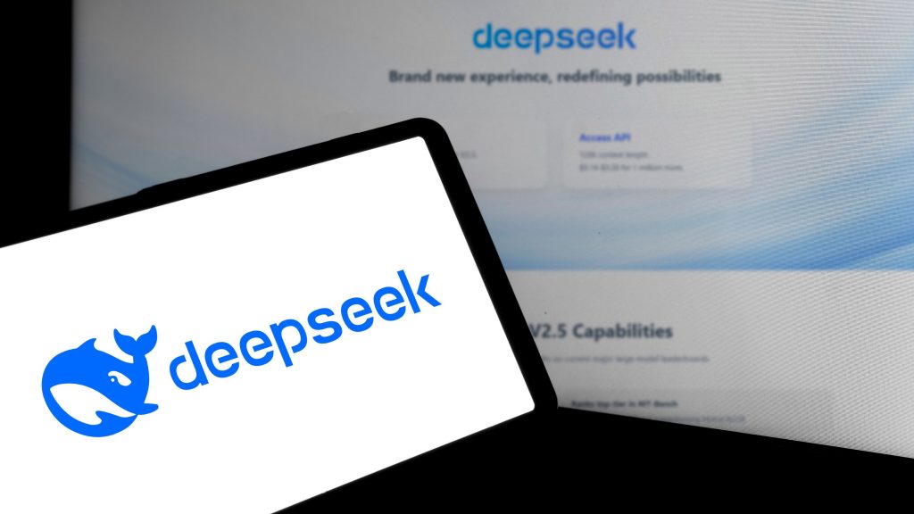 Celular com logomarca do DeepSeek colocado na frente de computador com página inicial da plataforma de inteligência artificial aberta num navegador