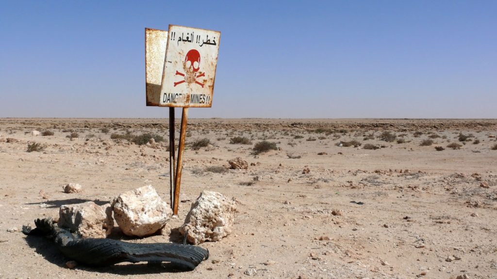 Duas placas colocadas uma de trás para outra em deserto avisando que existem minas terrestres na região