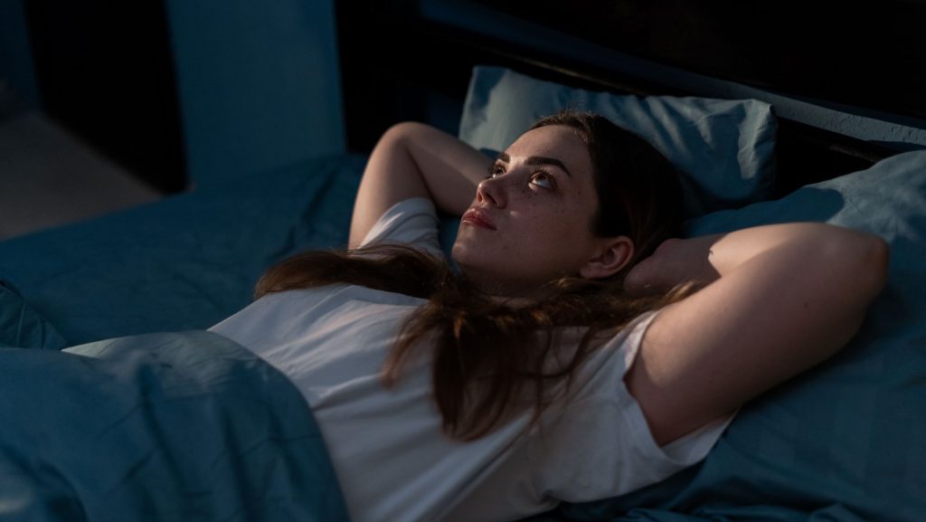 Mulher deitada na cama olhando para o teto com os braços cruzados atrás da cabeça