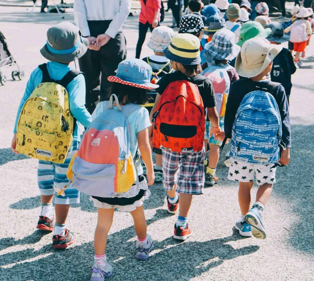 imagem mostra várias crianças andando para a escola com uma mochila nas costas