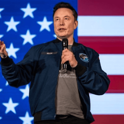 Elon Musk discursando; atrás, a bandeira dos Estados Unidos