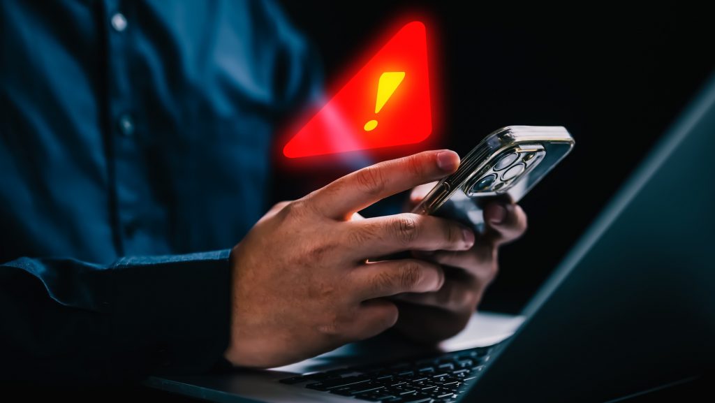 Símbolo de alerta acima de um celular que está sendo usado