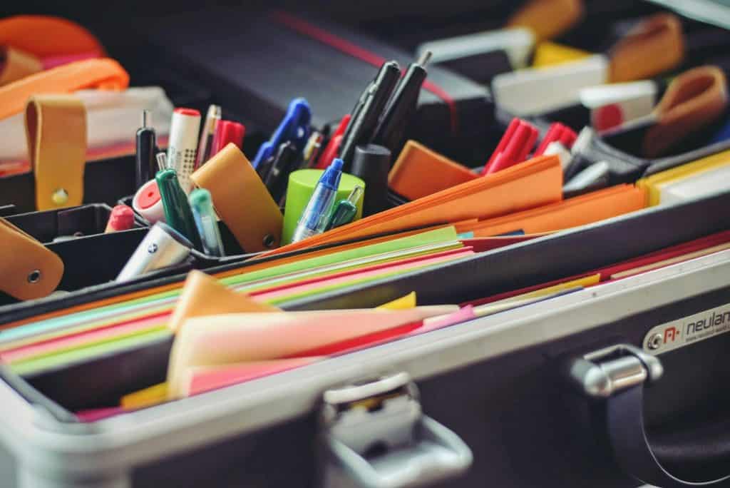 imagem mostra itens de papelaria, como canetas, marca texto, cola em bastão, post-its e muito mais