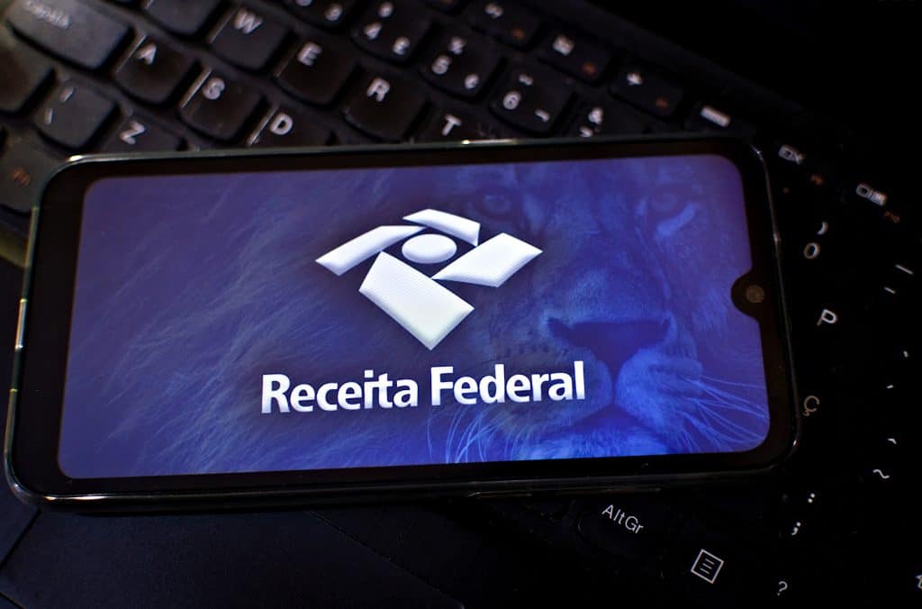 Logo da Receita Federal em um smartphone, que está em cima de um teclado de notebook