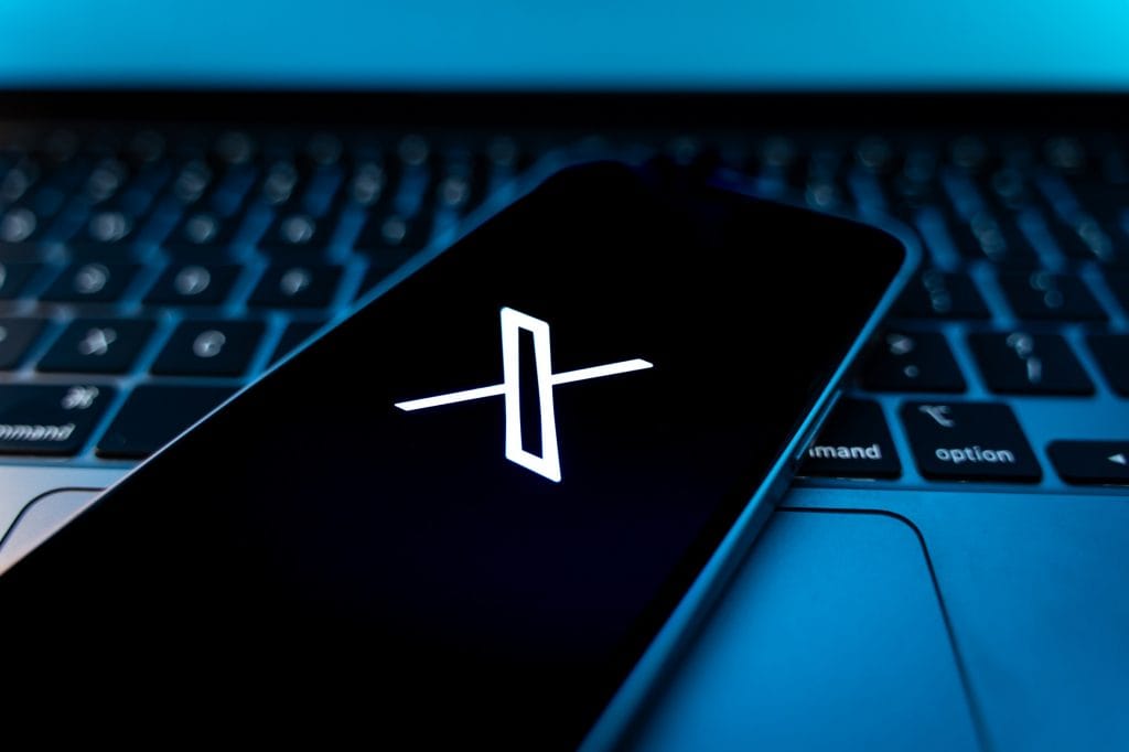 Logo do X em smartphone que está em cima de um notebook