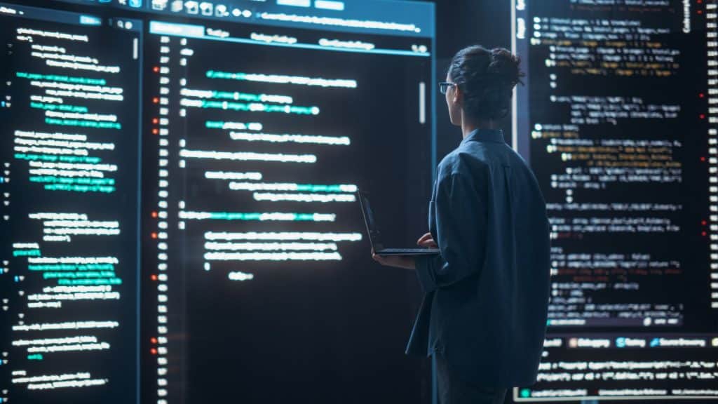 Imagem de uma Programadora Trabalhando em uma Sala de Controle de Monitoramento, Cercada por Grandes Telas Exibindo Linhas de Código de Linguagem de Programação. Retrato de uma Mulher Criando um Software, Programando.