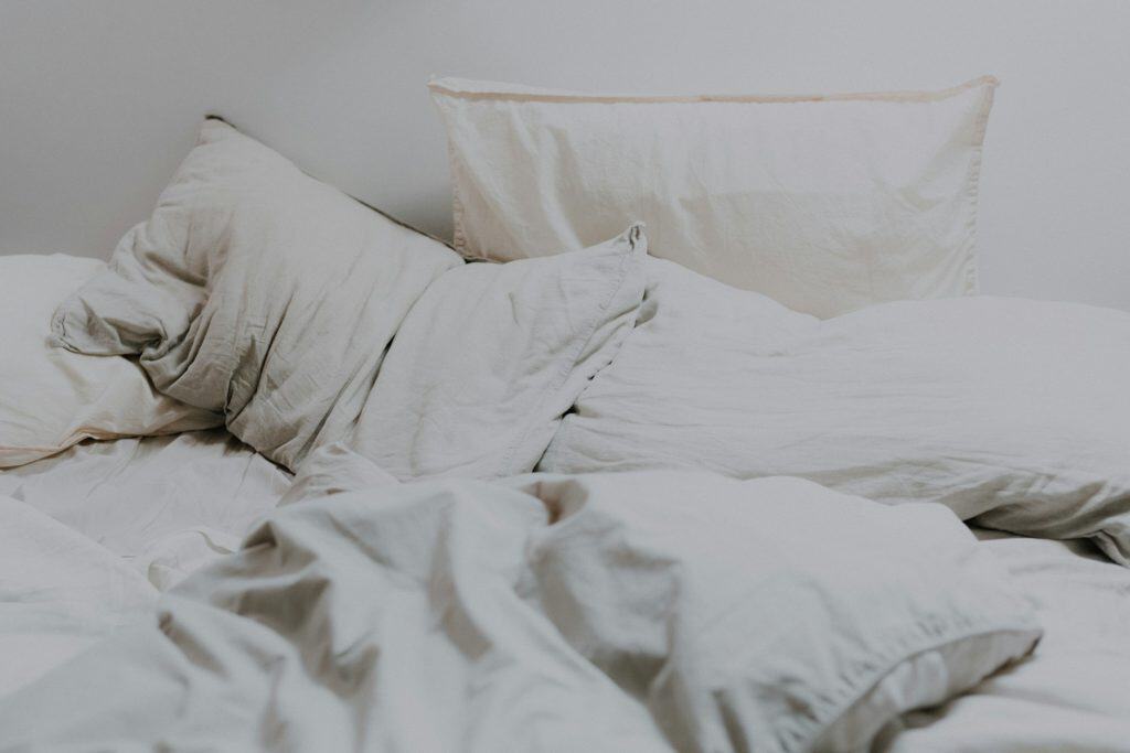 Cama bagunçada com lençóis e travesseiros brancos