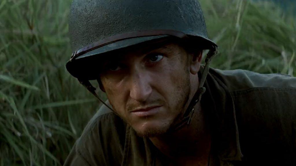 imagem mostra homem no meio de um campo de guerra, usando um chapéu à prova de bala