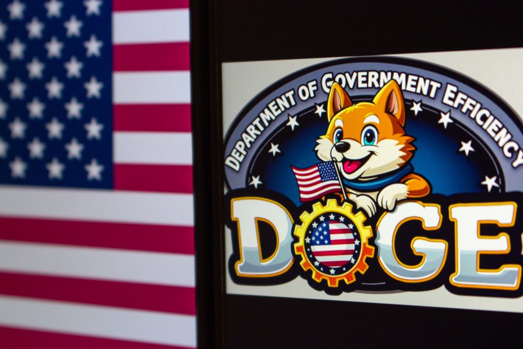 Logo do DOGE em uma tela, ao lado da bandeira dos EUA