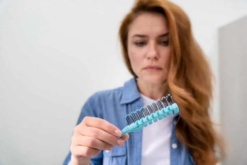 mulher olhando a escova com fios de cabelo