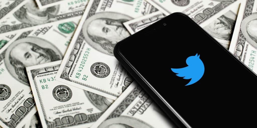 celular com o logo do Twitter cercado de notas de dólares
