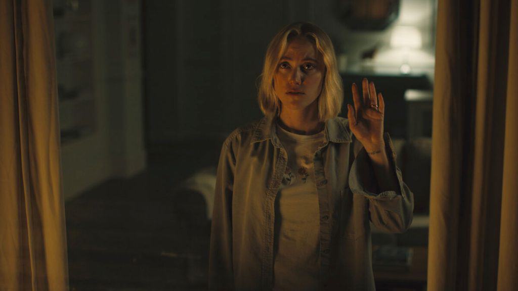 cena do filme O OBSERVADOR em que uma mulher está assustada, levantando a mão direita para cima