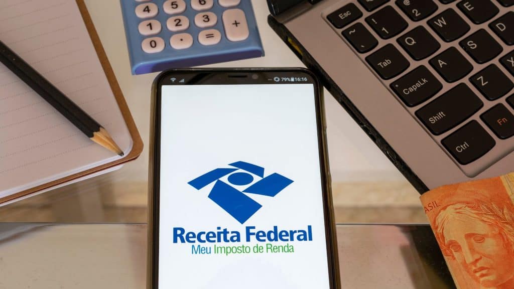 Celular com imposto de renda, Receita Federal, caderno, lápis, calculadora, caderno e moeda brasileira. Declaração de imposto de renda.