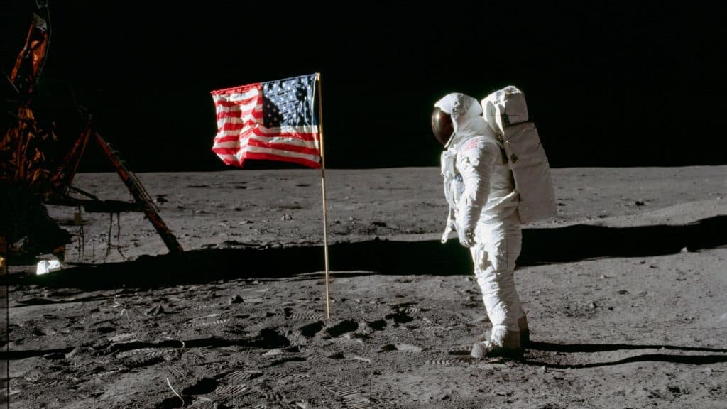 Bandeira dos Estados Unidos tremulando na superfície Lua enquanto astronauta está de pé ao lado dela