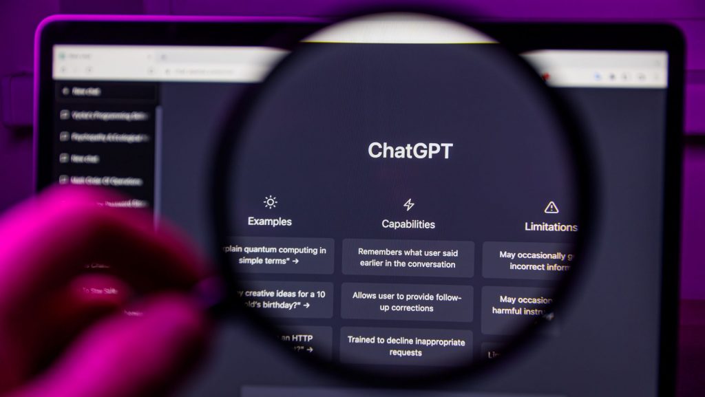 Foto estilo POV de pessoa segurando lupa sobre tela de notebook com ChatGPT aberto