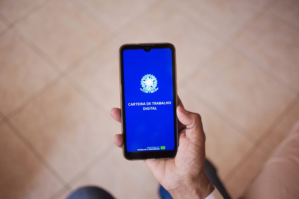 Tela inicial da Carteira de Trabalho Digital em um smartphone, que está sendo segurado por uma pessoa