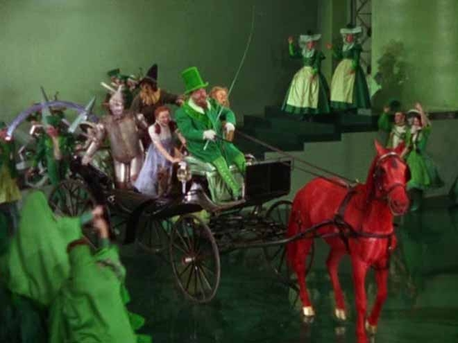cena de O mágico de oz com um cavalo vermelho e os outros personagens com roupa verde