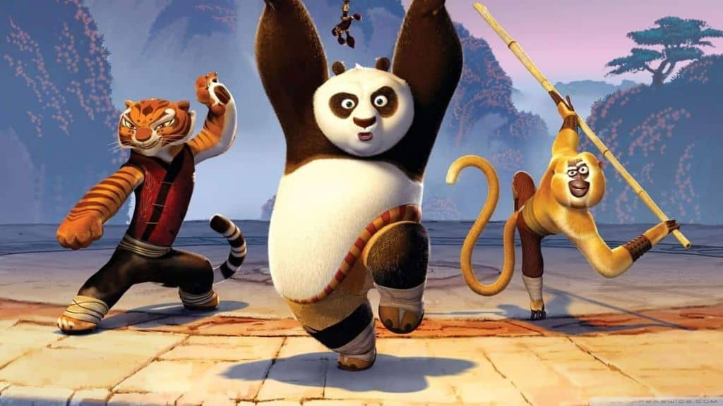 Três personagens de animação em ação: um panda ao centro, uma tigresa à esquerda e um macaco à direita segurando um bastão, todos em poses de luta em um cenário ao ar livre