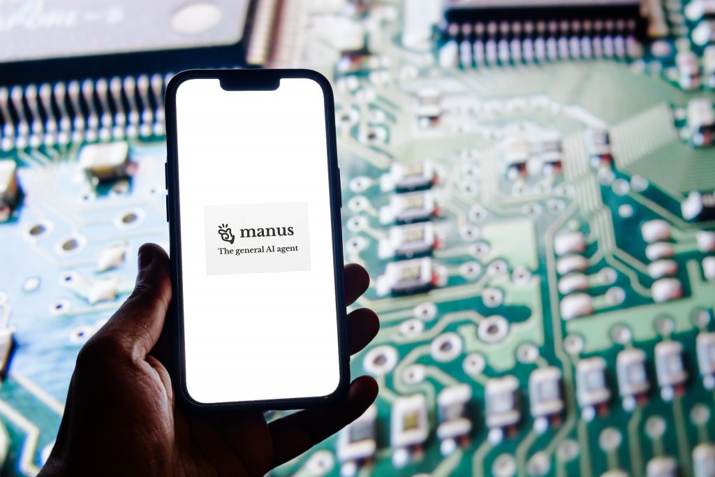 Ao fundo, placa-mãe; à frente, mão segurando smartphone com o logo da Manus