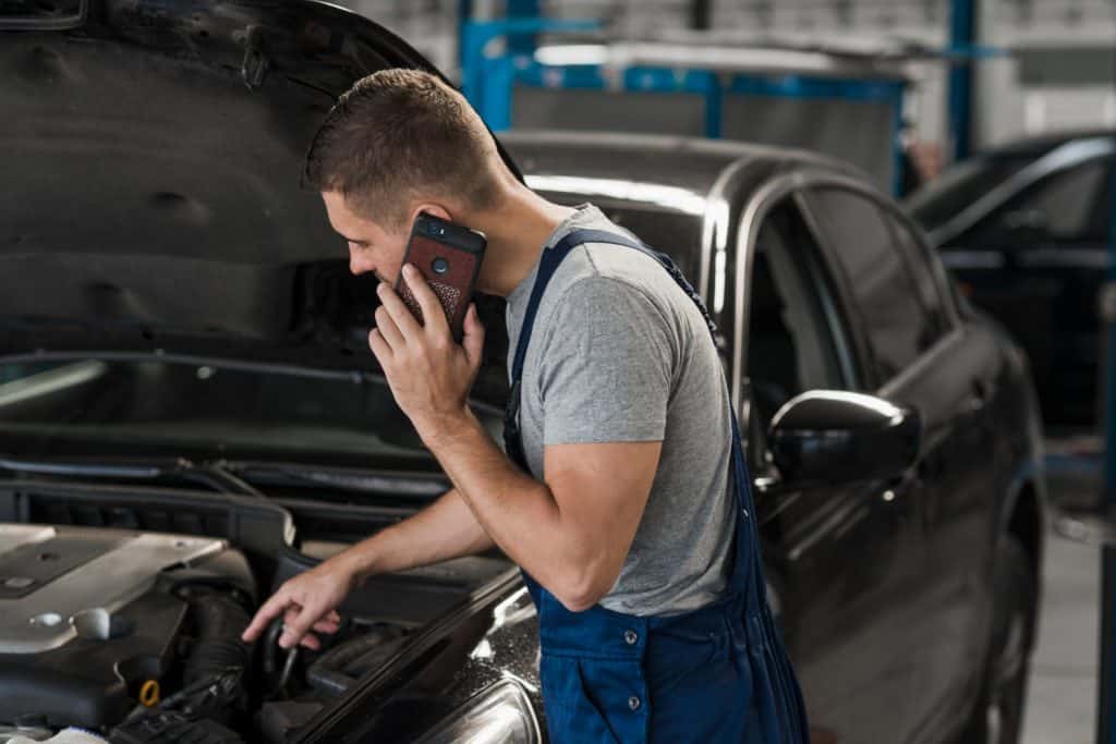 homem com celular na orelha e um carro com o capo do motor aberto