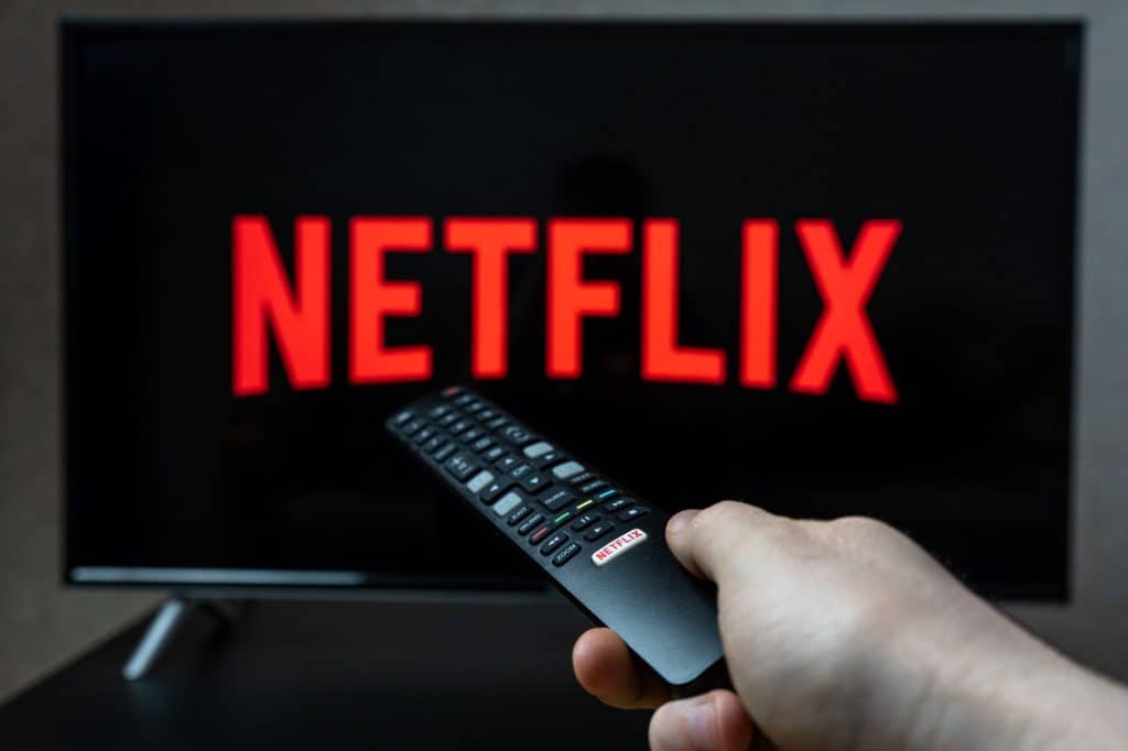 Logo da Netflix em uma TV; à frente, uma pessoa segurando um controle remoto