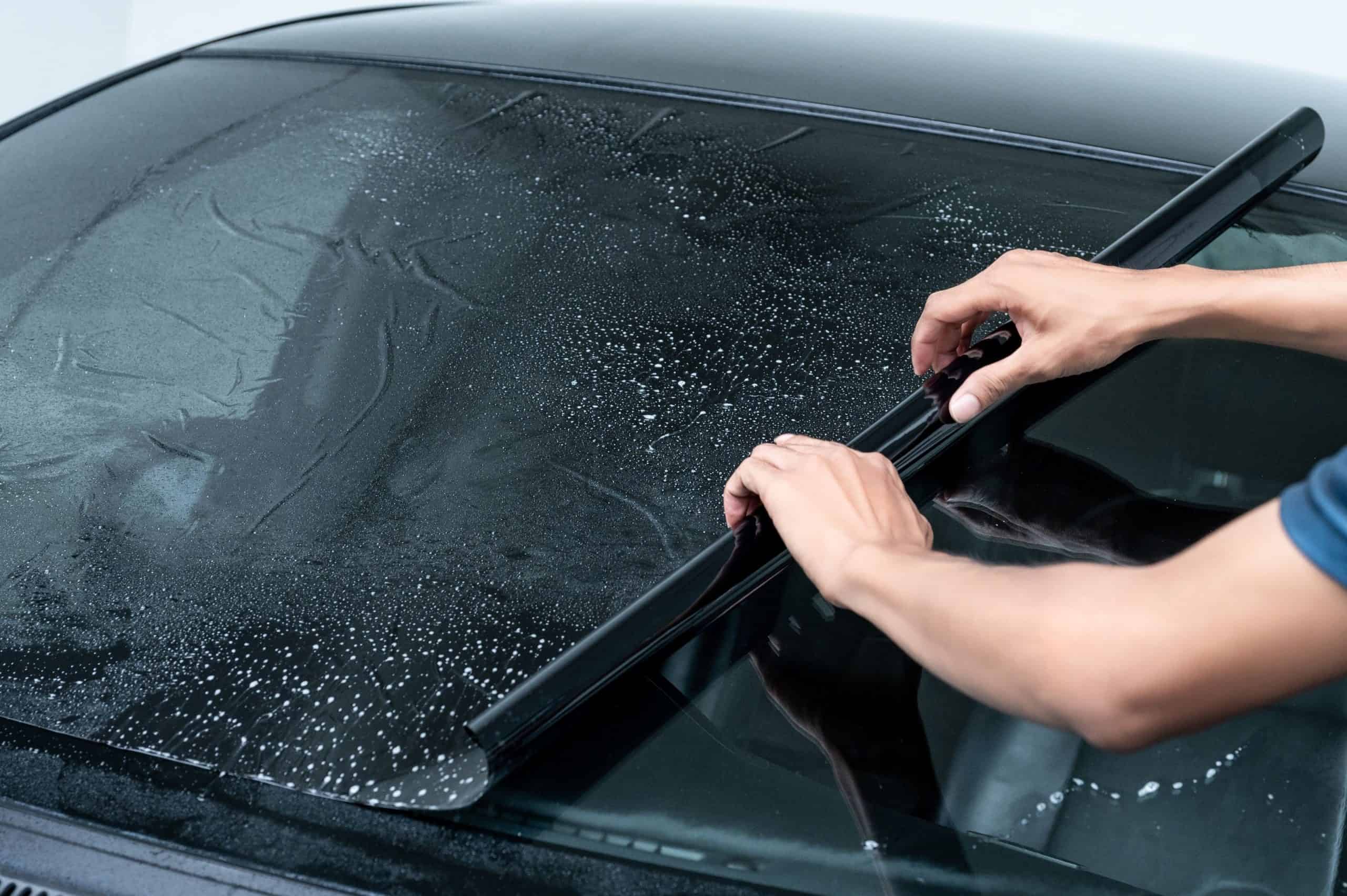 Trabalhador especialista em automóveis masculino aplicando manualmente película de janela de carro na superfície do vidro do para-brisa dianteiro