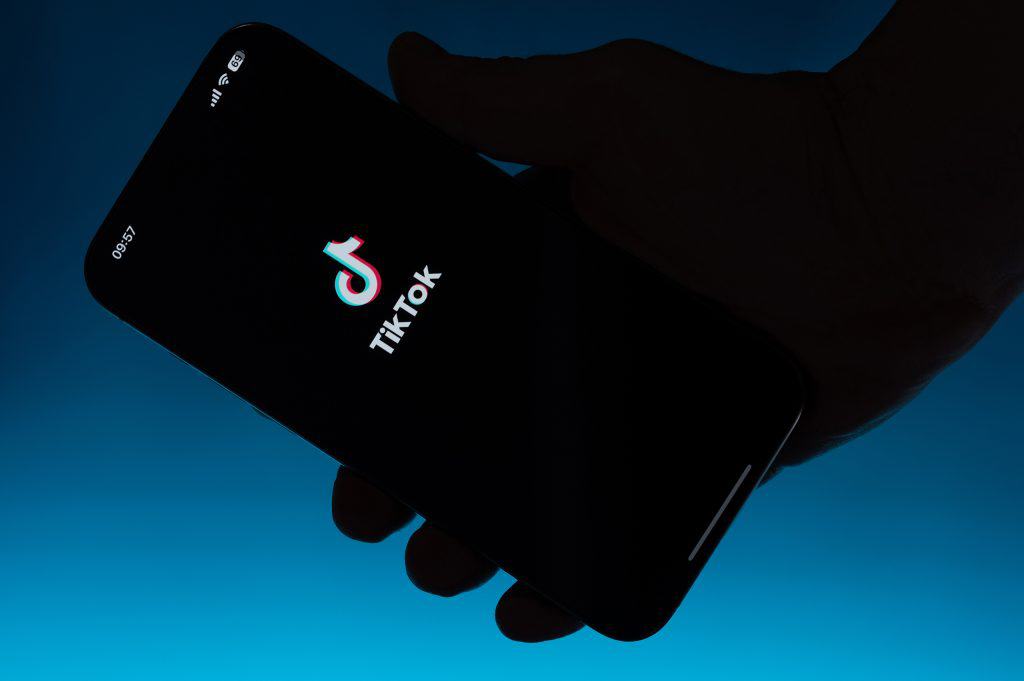 Logo do TikTok em um smartphone que está sendo segurado; ao fundo, um fundo azul