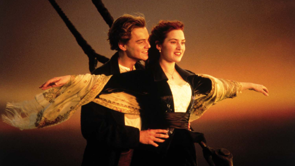 Cena icônica do filme Titanic, em que um jovem casal está na proa do navio ao pôr do sol. A mulher estende os braços enquanto o homem a segura por trás, transmitindo uma sensação de liberdade e romance