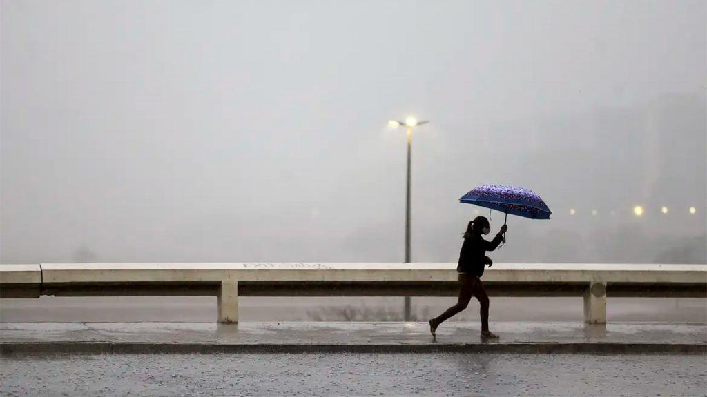 Mulher andando na chuva com guarda-chuva aberto
