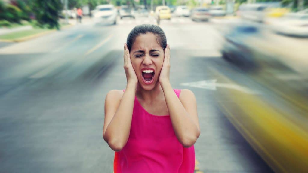 Retrato de mulher de pé ainda no meio de uma rua com carros passando rápido, gritando estressado e frustrado