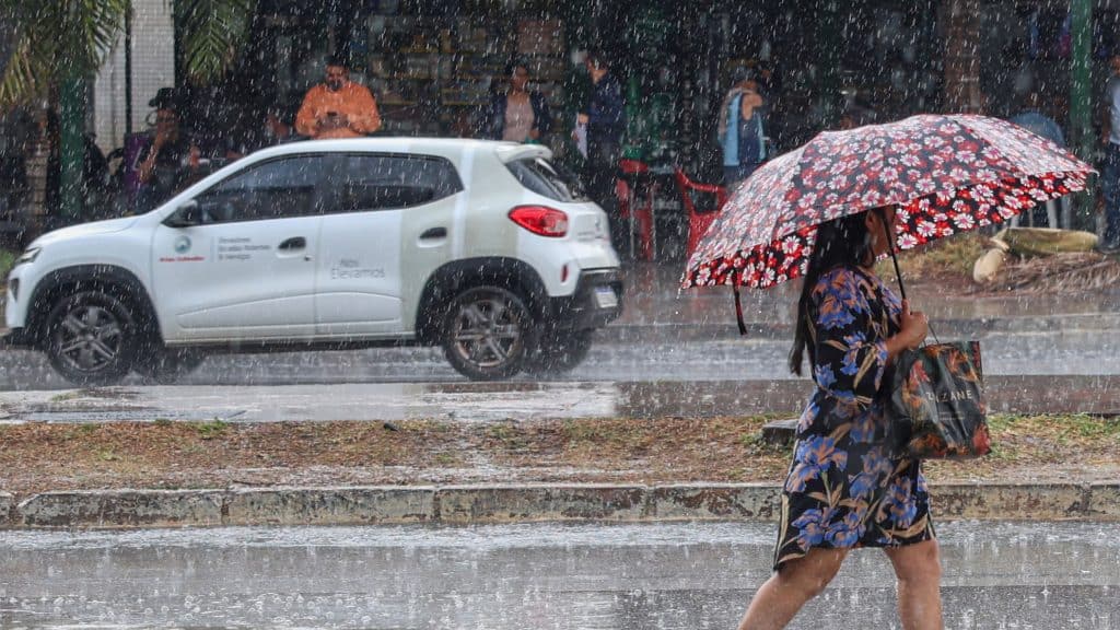 Mulher andando na chuva com guarda-chuva aberto em avenida