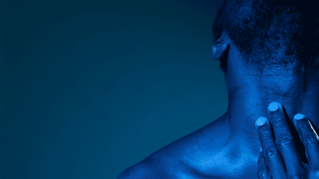 Imagem de um homem com a pele em tom azul intenso devido à iluminação. O fundo é escuro e uniforme