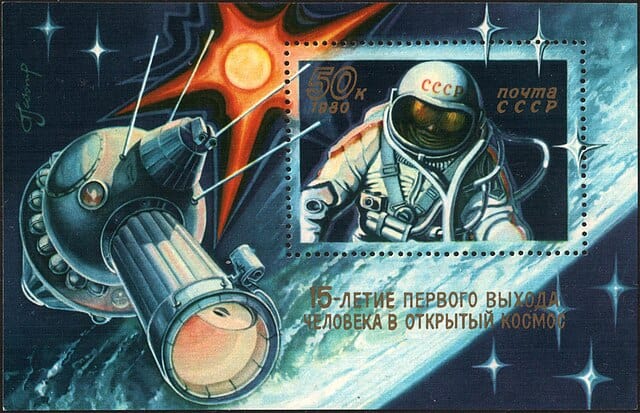 Selo postal da União Soviética mostrando o cosmonauta Alexei Leonov no espaço, com o Sol, a nave Voskhod-2 e uma assinatura estilizada; lançado em 1980 para marcar os 15 anos da primeira caminhada espacial.