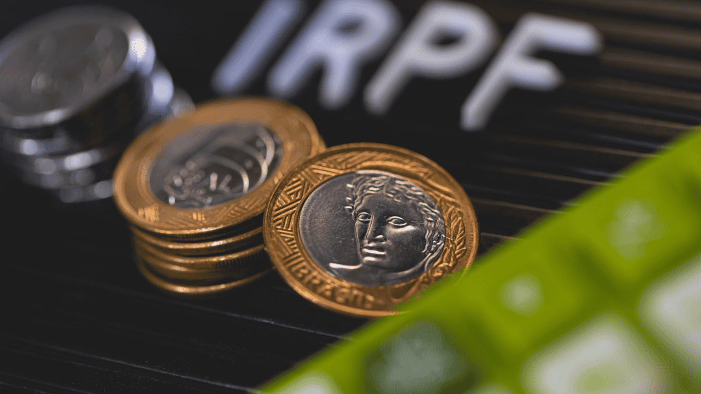Montes de moedas brasileiras em macrofotografia e as iniciais IRPF em uma moldura com letras referindo-se ao Imposto de Renda da Pessoa Física. Economia Brasileira