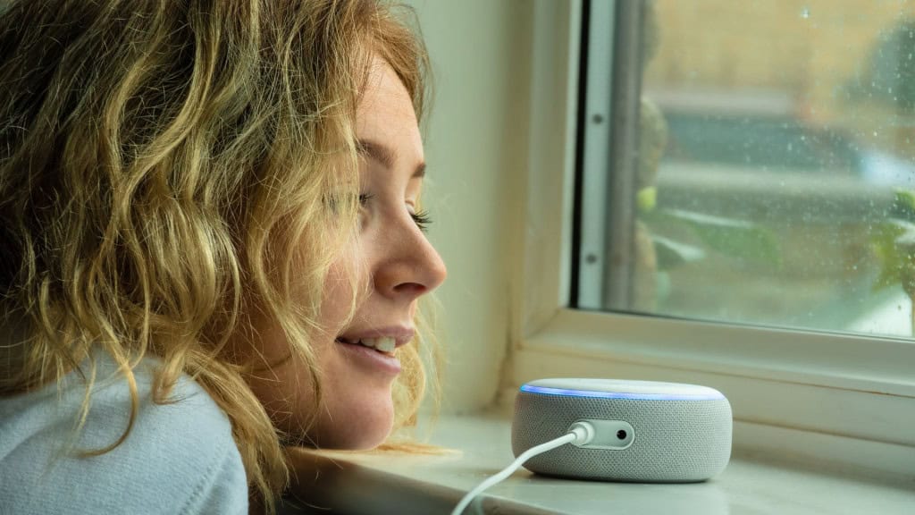 MOSTERTON INGLATERRA FEVEREIRO DE 2020 - Adolescente conversando com um Amazon Alexa Echo Dot perto de uma janela em um dia chuvoso