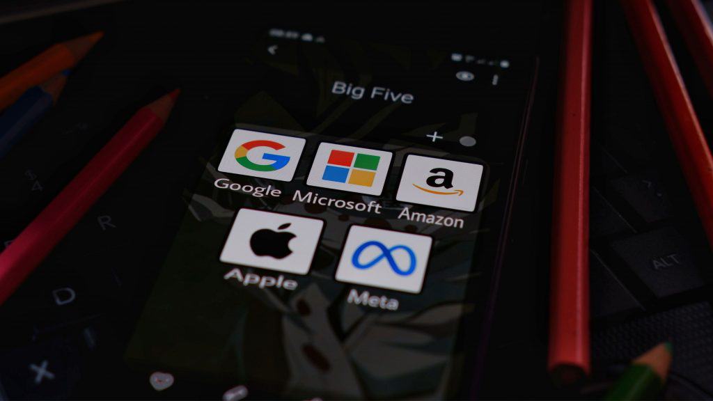Ícones de aplicativos das big techs Google, Microsoft, Amazon, Apple e Meta numa pasta na tela inicial de um iPhone