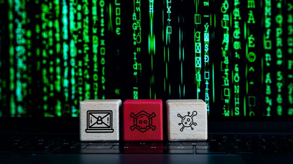 Cubinhos com desenhos de vírus, perigo e desinformação colocados em cima de teclado de notebook cuja tela mostra imagem de caracteres verdes na vertical estilo Matrix