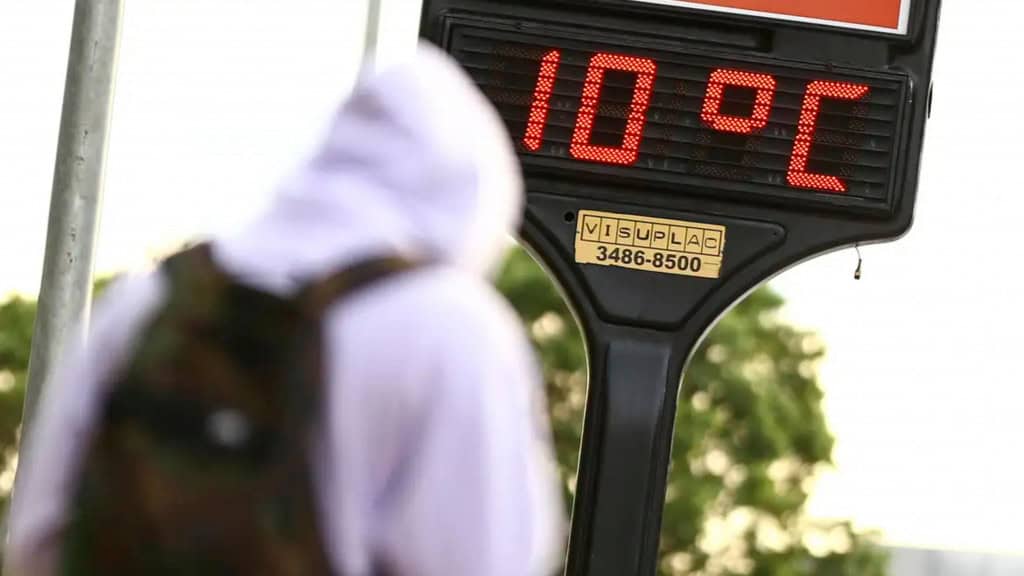 Pessoa de moletom passando por termômetro que marca 10 graus Celsius em dia frio