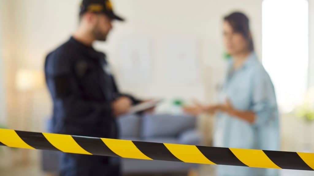 A cena do crime do acidente é cercada com uma fita com uma jovem vítima do crime em pé com um policial homem interrogando-a depois de um roubo em casa. Roubo, conceito de violência doméstica.