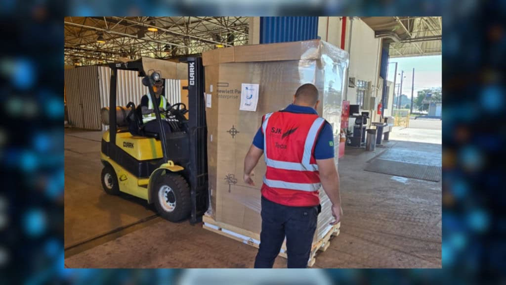 Homem dirigindo empilhadeira carregando caixa com novo supercomputador do Inpe enquanto outro homem o auxilia em armazém
