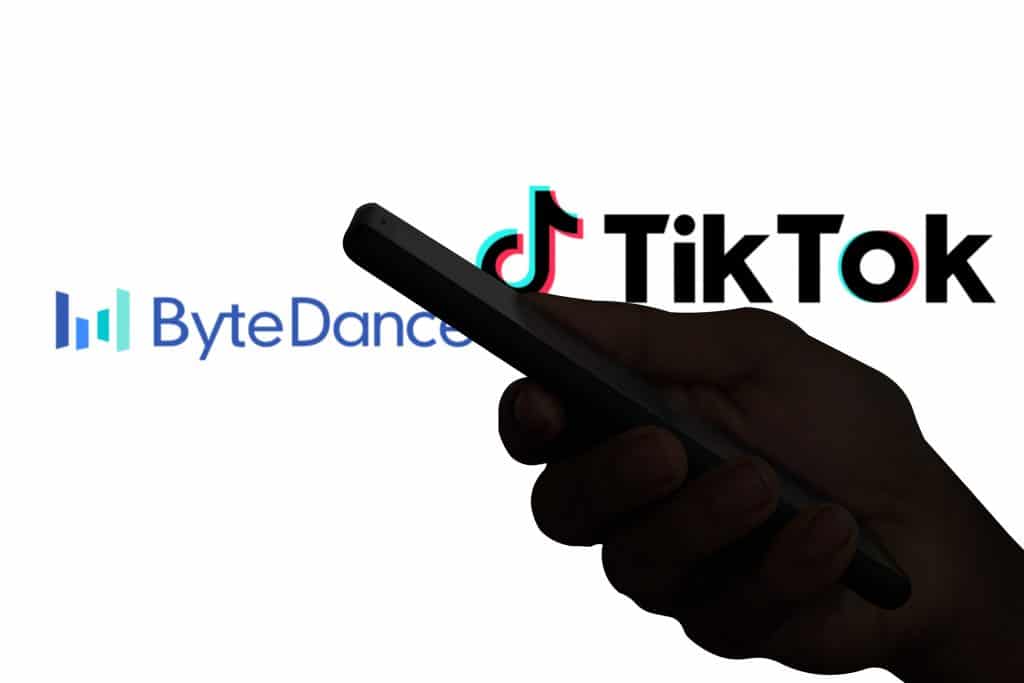 Logos de TikTok e ByteDance divididos por uma sobra de uma mão segurando um smartphone
