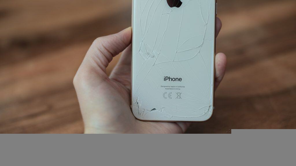 imagem mostra uma pessoa segurando um iphone sobre o chão. a traseira do aparelho encontra-se rachada