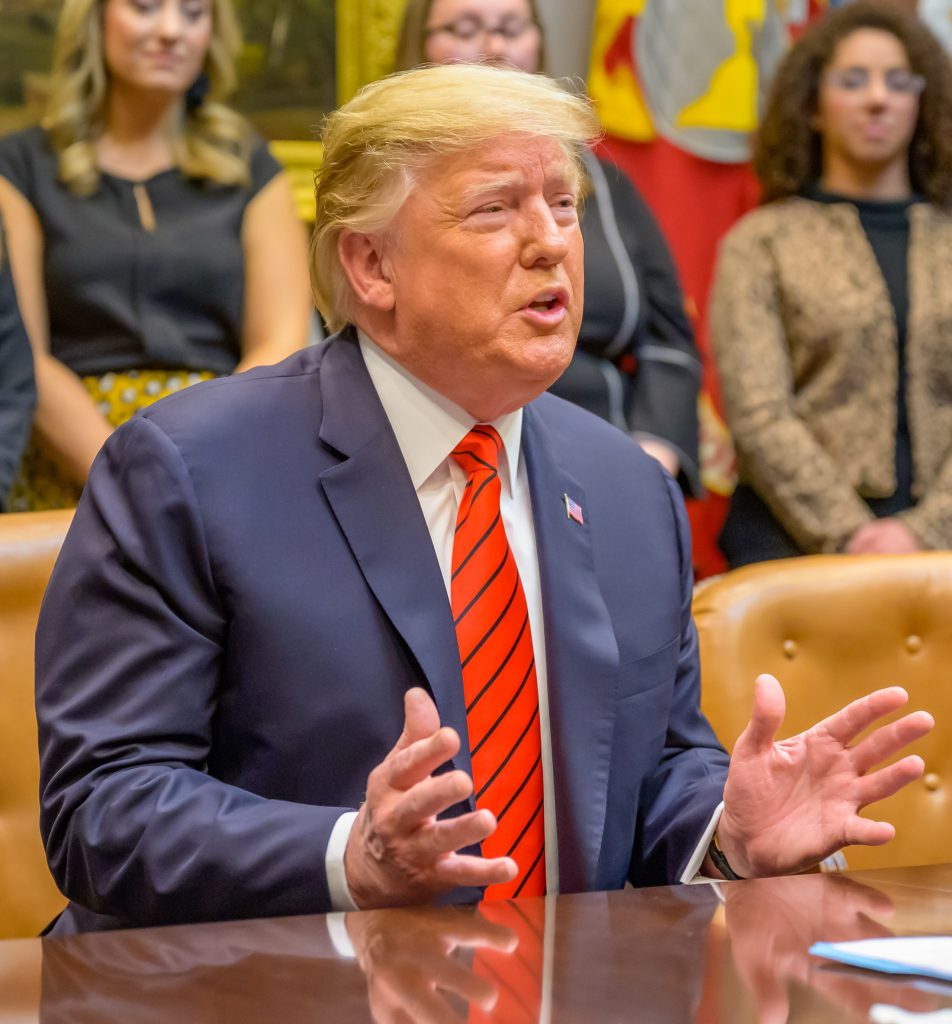 Donald Trump em uma mesa falando e gesticulando